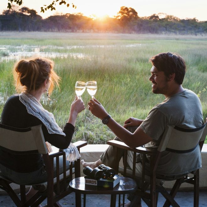 Couple making wine toast at sunset at safari lodge, Kafue National Park, Zambia