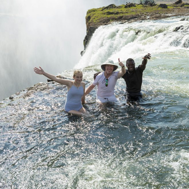 Three people standing in the waters of the Devil's Pool, Victoria Falls.